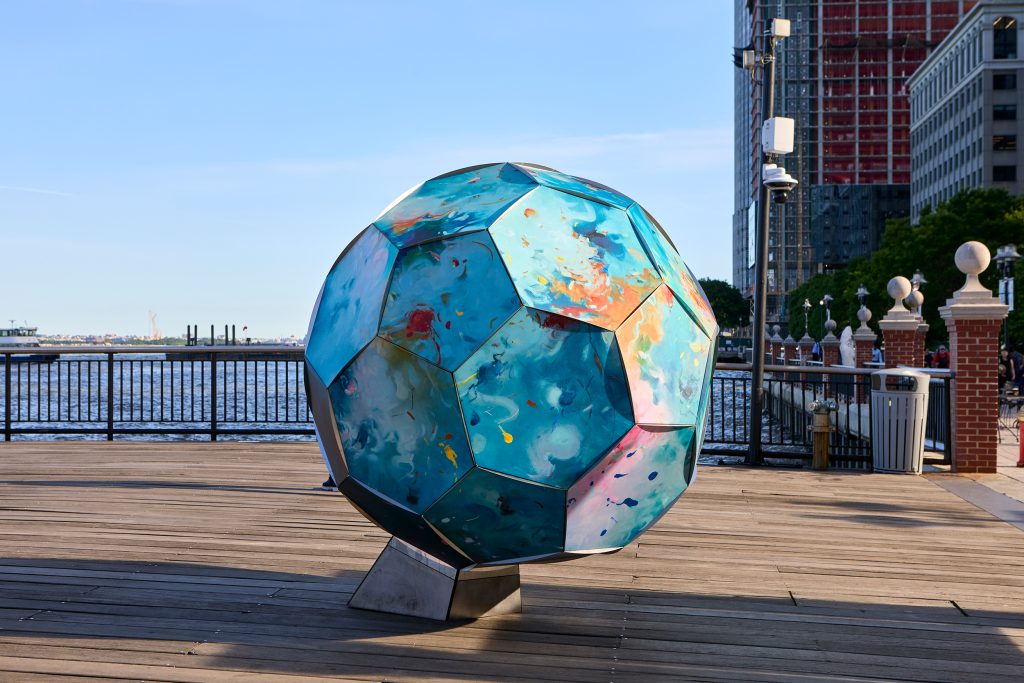 large soccer ball sculpture covered in abstract floral paintings on a wooden pier in the sunshine