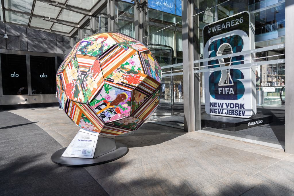 soccer ball sculpture with colorful anime-like figures on a sidewalk in front of a sign for the 2026 FIFA World Cup