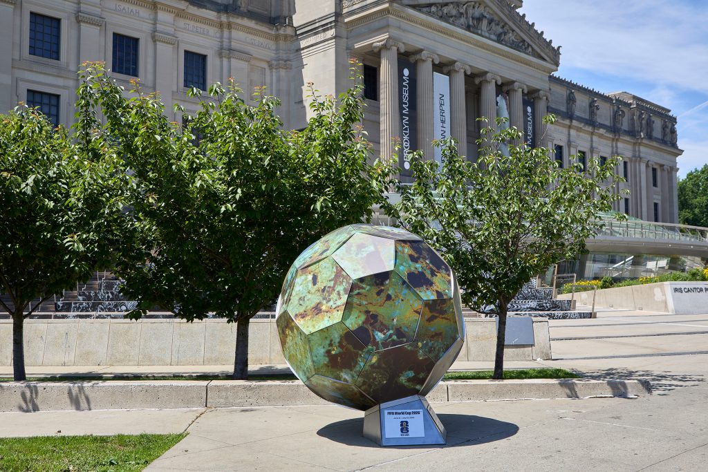 Large soccer ball sculpture painted to look like a lichen covered rock in front of the Brooklyn Museum