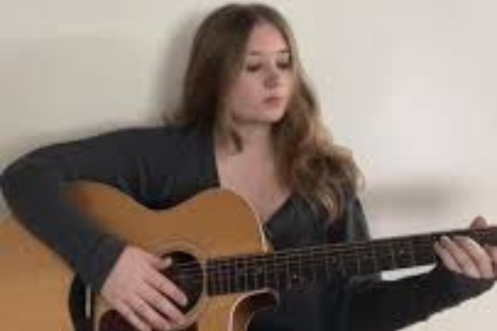 ARTS 14C Fellowship Artist Torrin Murray playing an acoustic guitar while seated indoors against a light-colored background.