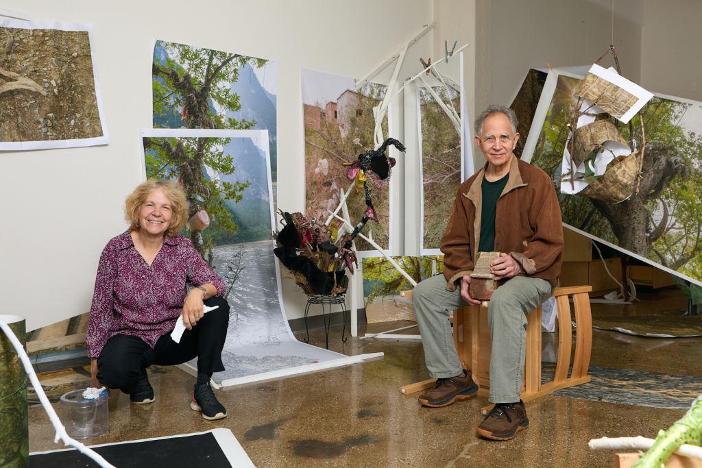 Sculptor Wendy Hirschberg and photographer Edward Fausty pose in their ARTS 14C studio amid large-scale photographs, sculptural elements, and an immersive mixed-media installation inspired by natural landscapes.